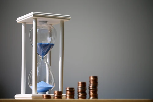 Image of an hourglass with coins stacked next to it