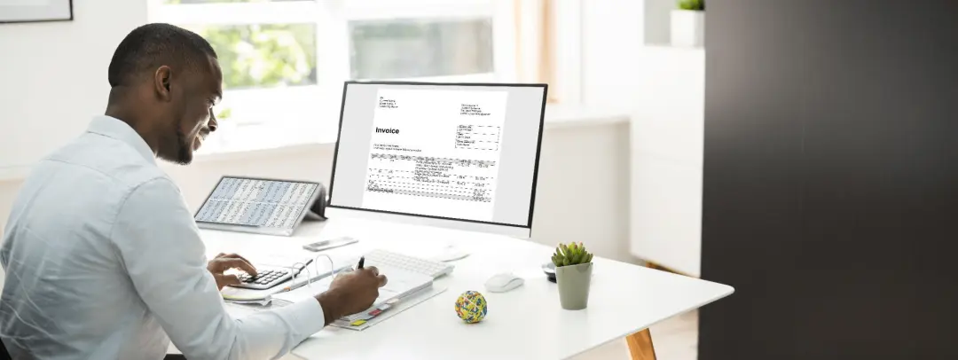 A man sitting at a desk filing an invoice on a computer