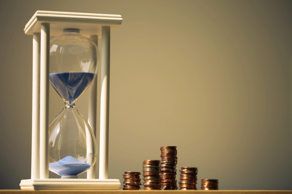 An hourglass with a stack of coins next to it