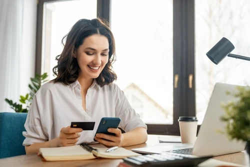 Image of a young woman smiling while making a payment on her phone.