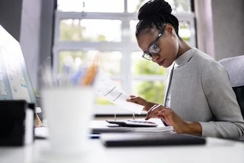 Woman typing on a calculator and holding a sheet of paper