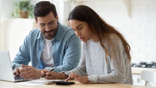 Man and woman sitting at a computer and working on a calculator