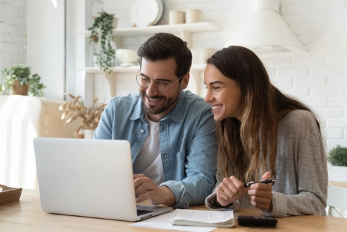 A man and woman sitting in front of a computer at their dining room table