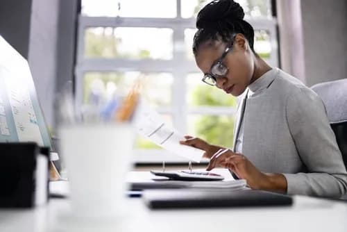 Woman typing on a calculator and holding a sheet of paper